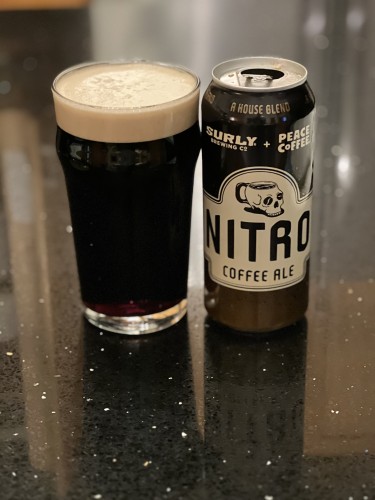 A can of Surly Brewing Nitro Coffee ale and a pint glass of the same. The can is dark brown with tan and brown lettering and a prominent Skull-shaped coffee cup above the large word “NITRO”