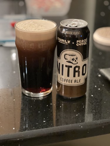 A dark brown point cannot Surly Brewing Nito Coffee Ale is boldly lettered in tan shades and features a coffee cup shaped like a skull. A pint glass is to the left still sheeting its nitro from a hard pour.