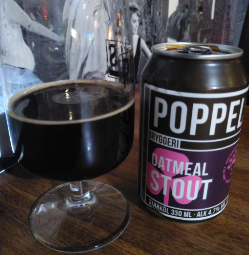One half-full glass of oatmeal stout on a eooden table, with the can from Poppels brewery beside it. Film pictures in the background.
