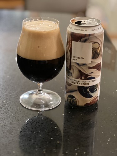 An artfully decorated pint beer can from UntitledArt brewery. A hard pour has left a tulip glass half full of beer and half full of foamy rich tan head. 