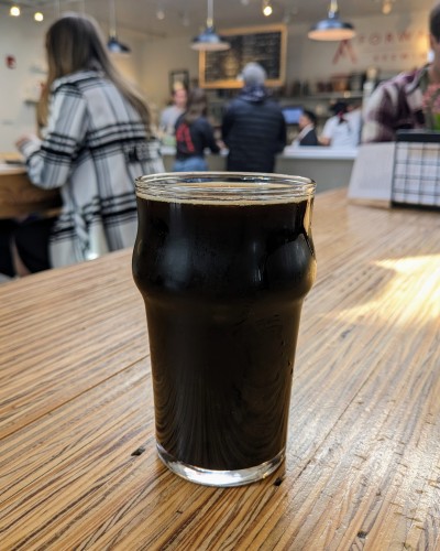 A black beer in a glass. Patrons and bar in the background.