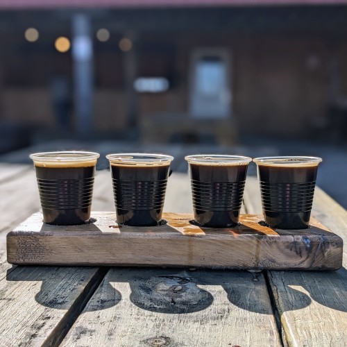 A flight of four black beers, in a wooden flight holder, on a wooden picnic table.