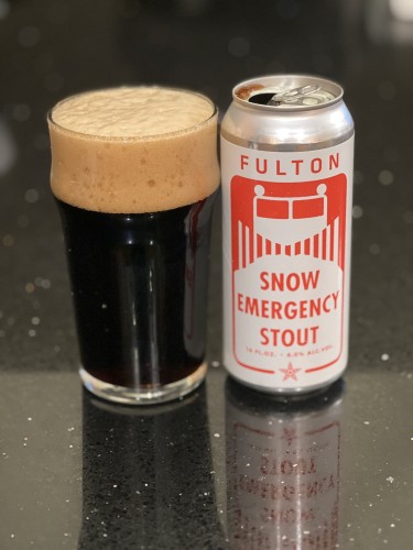 A pint glass of dark beer with a tall tan head next to its can, emblazoned with a red and white snow plow on a white background.