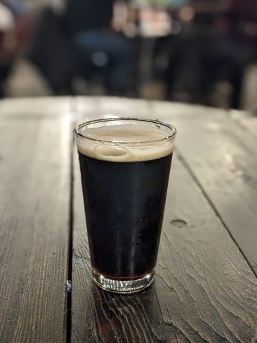 Black beer in a pint glass on a wood table.