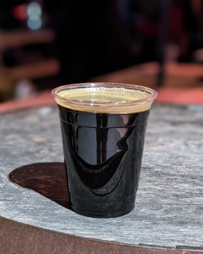 A black beer in a clear plastic cup on a wooden barrel.