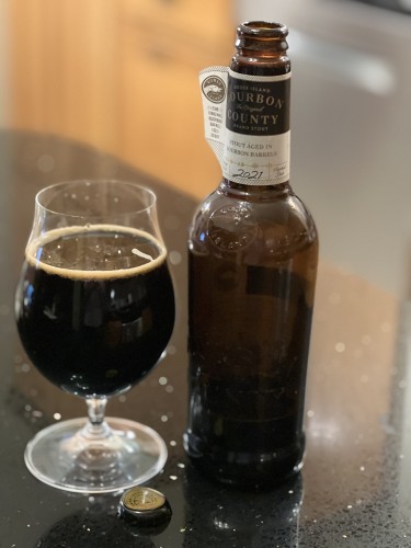 A 750ml brown bottle of Goose Island Bourbon County stout beer bears only a neck label showing its 2021 vintage. A tulip glass of the rich brew is to the left.