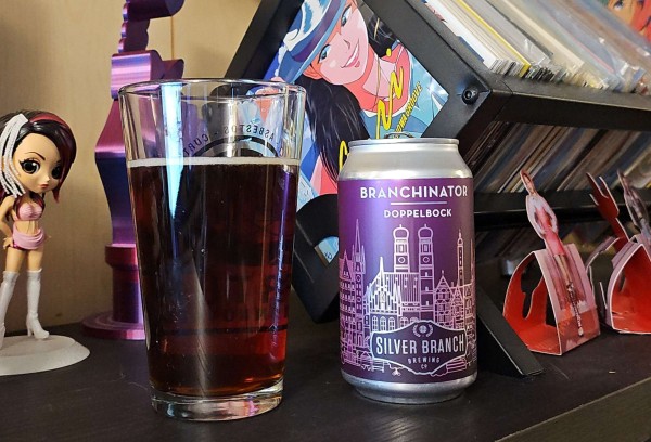 A pint glass filled with beer and a 12oz can sit on a shelf. A Koda Kumi QPosqet is in the background along with some 7inch vinyl in a rack. 