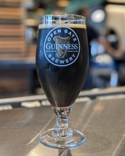 Black beer in a stemmed glass on a chrome bar. Guinness Open Gate Brewery logo on the glass.