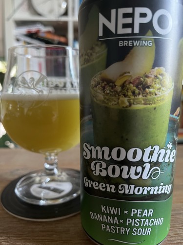 A can of NEPO Brewing Smoothie Bowl beer with the flavor "Green Morning" featuring kiwi, pear, banana, and pistachio is in the foreground. A glass with a hazy greenish beverage is in the background, sitting on a