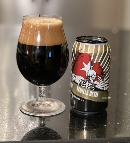 A tulip glass of dark beer with a thick tan head is once left of a red, gold and white can white a Skeleton carrying a furled red flag with a large white star on it