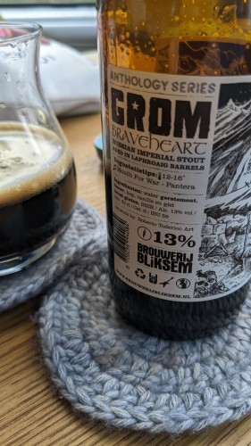 Bottle of Grom Braveheart stout on a crochet coaster next to the poured glass on the same coaster.