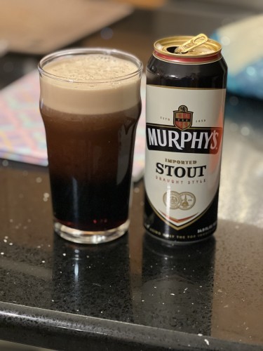 A pint glass of Murphys stout, sheeting nitro to a rich tan head. The open can is to the right.