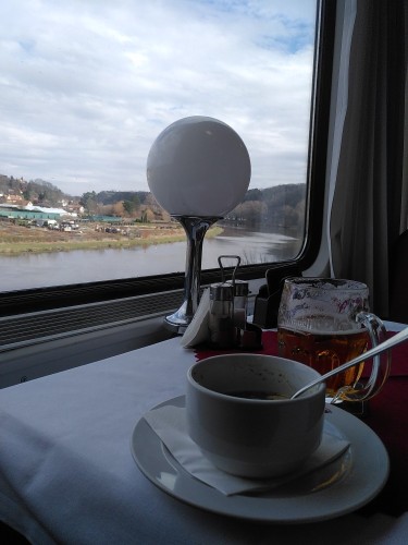 Picture of soup and a beer glass on a train restaurant wagon/coach against the background of a train window with a view over the Vltava (Moldau) river.