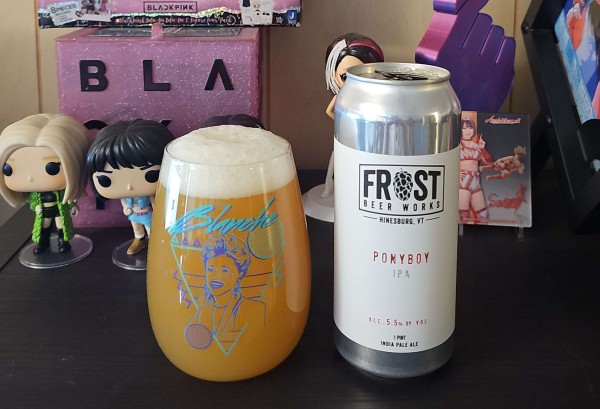 A glass filled with beer and a 16oz can sitting on a shelf. The glass features Blanche of the Golden Girls, with 80s like design behind her. 