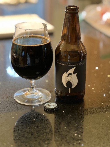 A bottle of Prairie Artisan Ales Vanilla Double Noir stout features a solid black background with a stylized flame with the shape of a woman in a low-backed dress inside it. 